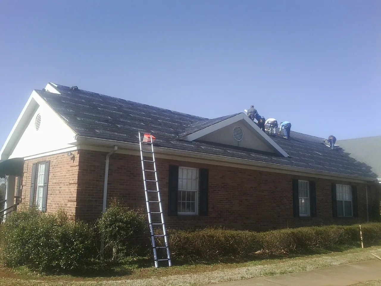 Crew tearing shingles off a brick ranch roof with a ladder set — Emergency Roof Repair work by our crew in South Bend