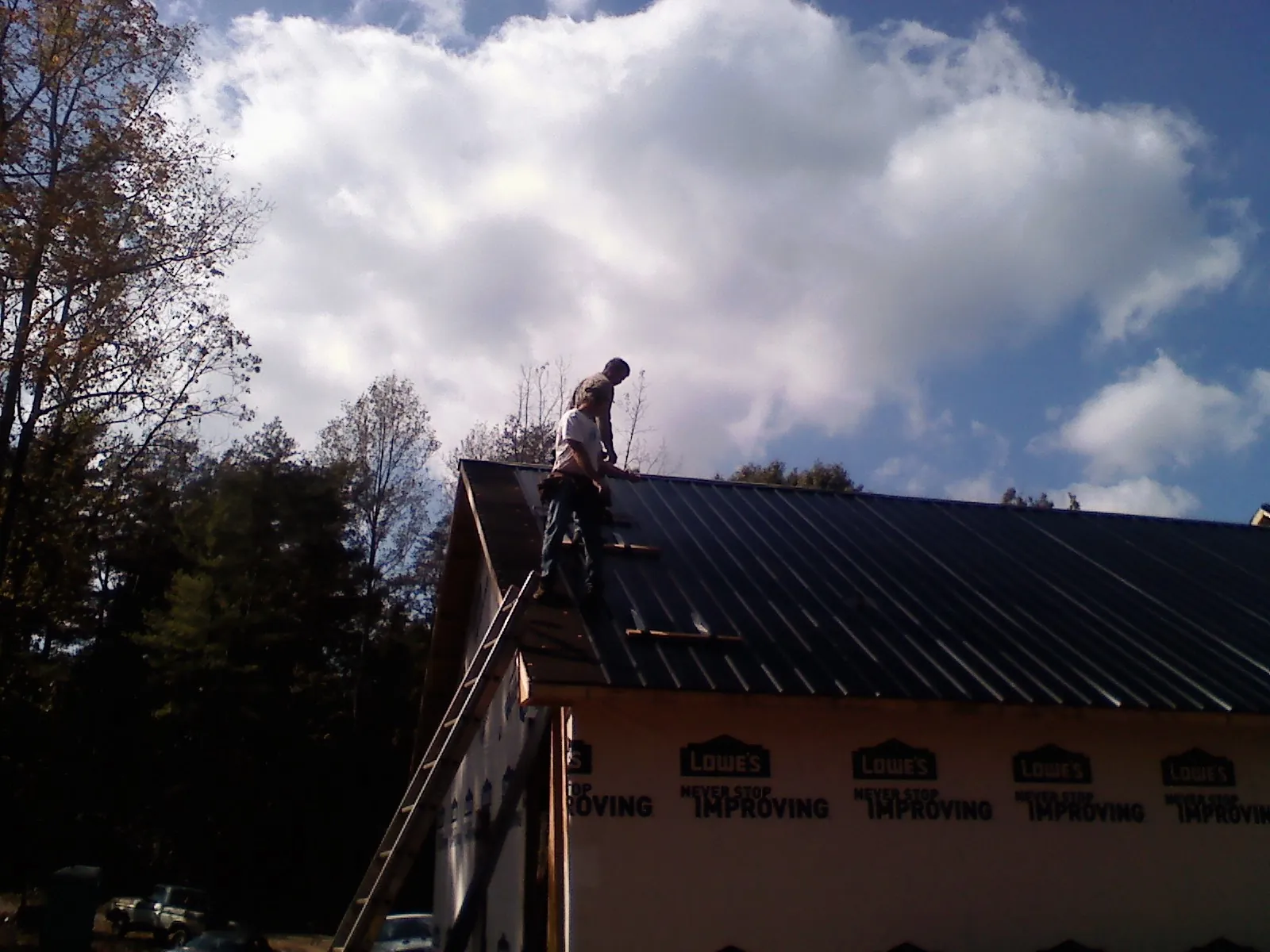 Roofer fastening dark metal panels high against a cloudy sky, from a Roof Inspection job in South Bend